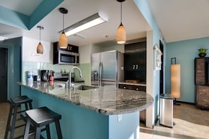 A modern kitchen with a central island, stainless steel appliances, and pendant lighting. - Coastal Comfort on the Beach with Free Seasonal Chairs, Pools & Sunset Views (Panama City Beach)
