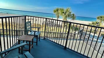 Un balcon avec vue sur la plage, une table en bois et deux chaises.