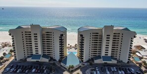 A beachfront hotel with two high-rise buildings, a parking lot, and a view of the ocean. - Coastal Comfort on the Beach with Free Seasonal Chairs, Pools & Sunset Views (Panama City Beach)