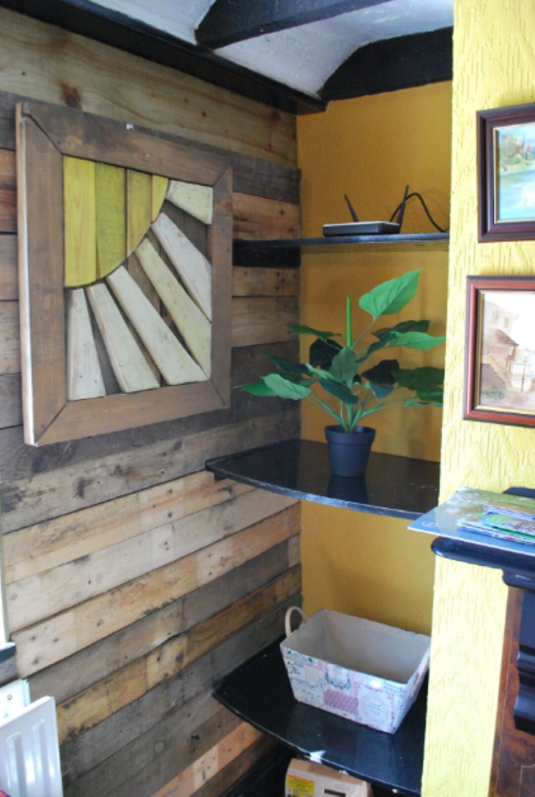 A room with a wooden wall, a black shelf with a potted plant, and a framed picture.