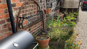 Un barbecue, un mur de briques et un jardin agrémenté de plantes et de fleurs en pot.