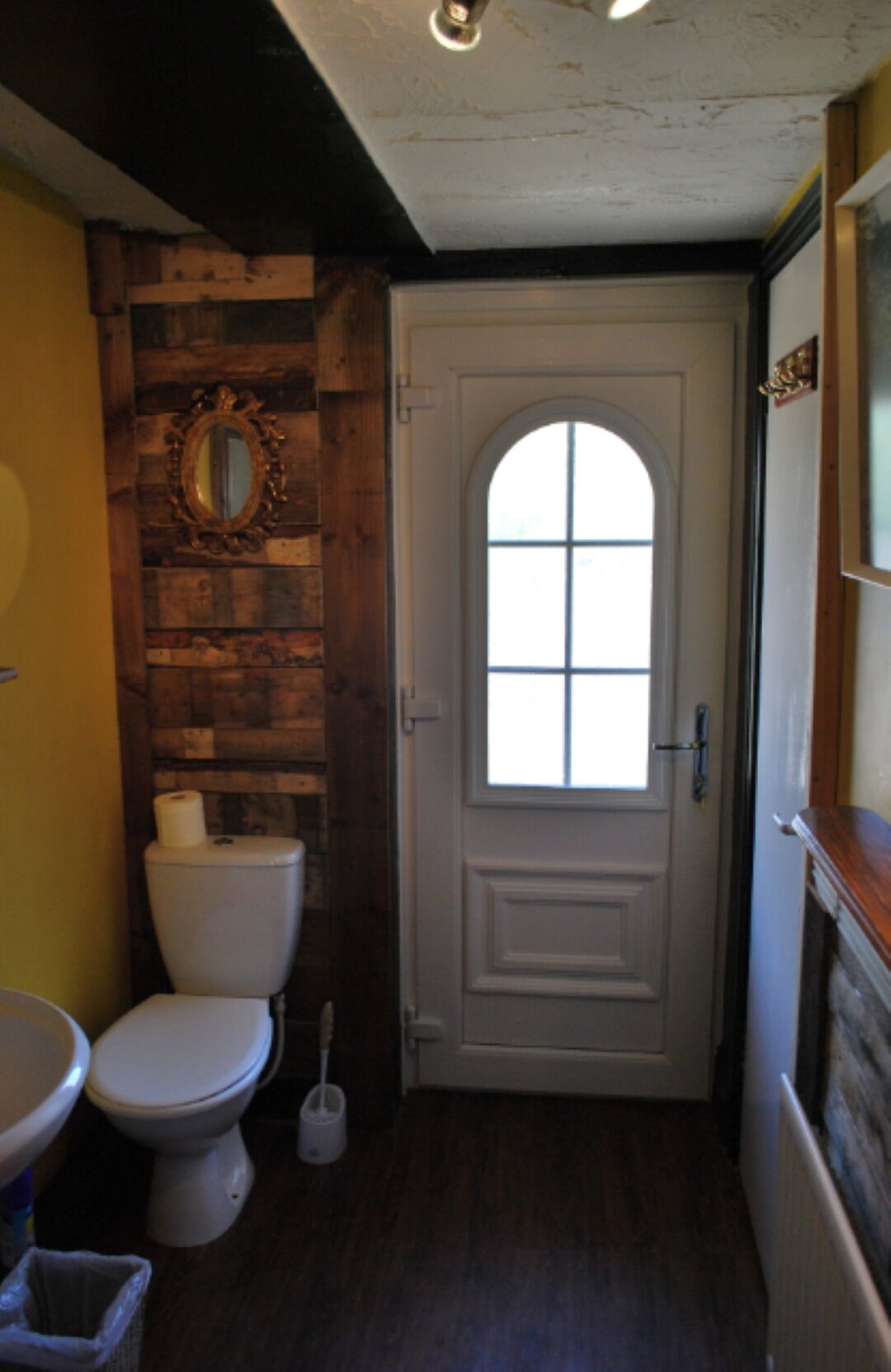 A bathroom with a wooden wall, a white door with a window, a toilet, and a sink.