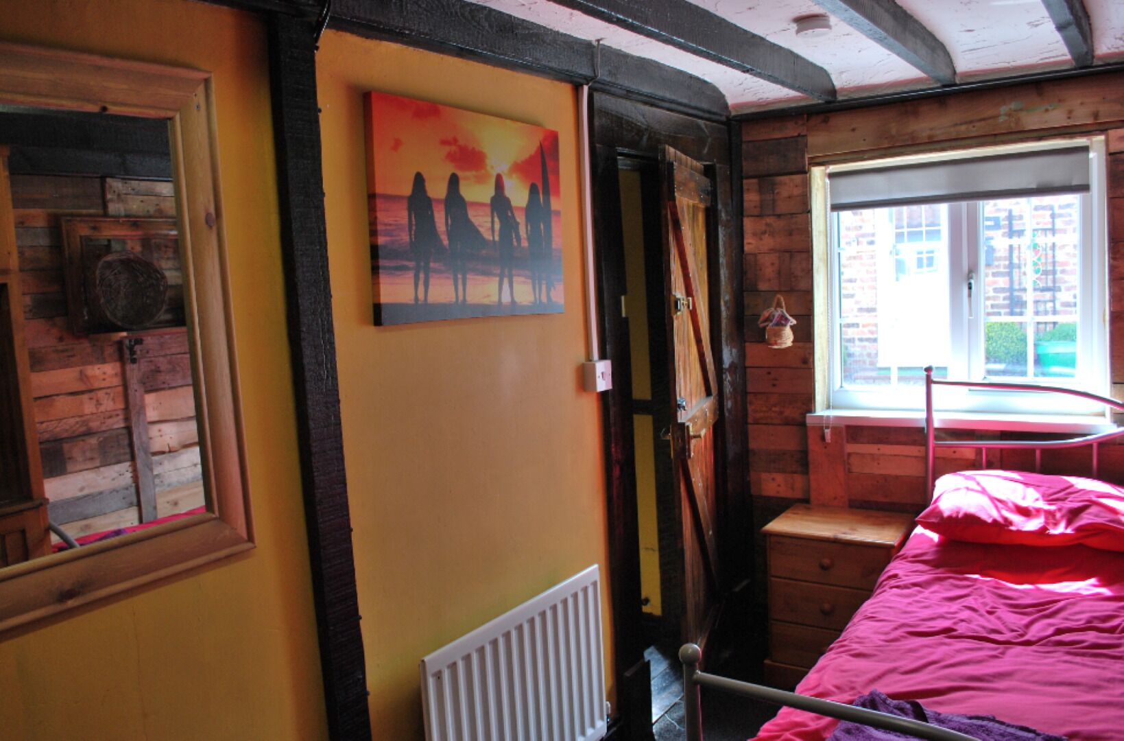 Een kamer met een bed, een raam, een radiator en een schilderij aan de muur.