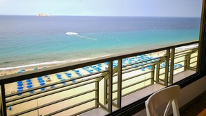 Un balcón con vista a la playa, con sombrillas azules y cielo despejado.