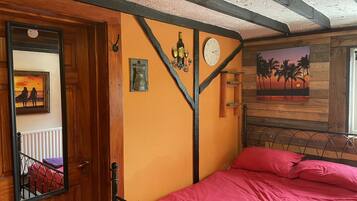 Una camera da letto con una porta in legno, un letto con lenzuola rosa, una sveglia appesa al muro e un quadro raffigurante una spiaggia.