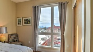 A hotel room with a large window, a bed, a chair, and a lamp. - 5th-Floor Condo | Balcony + Parking | Heart of AVL (Asheville)