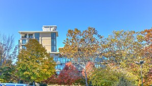 A modern building with a glass facade, surrounded by trees with autumn foliage. - 5th-Floor Condo | Balcony + Parking | Heart of AVL (Asheville)