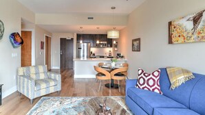 A modern living room with a blue sofa, patterned armchair, and a dining area with a round table and chairs. - 5th-Floor Condo | Balcony + Parking | Heart of AVL (Asheville)