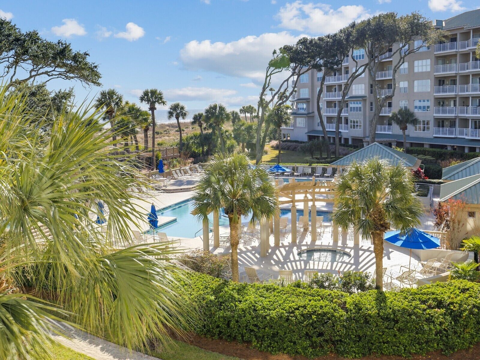 Un resort con piscina, palmeras y un edificio de varios pisos con balcones.