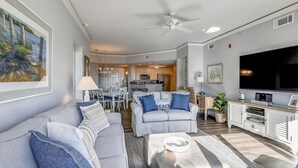 Un soggiorno moderno con un divano grigio, un tavolino da caffè e una TV. C'è una zona pranzo con tavolo e sedie, e una cucina sullo sfondo.