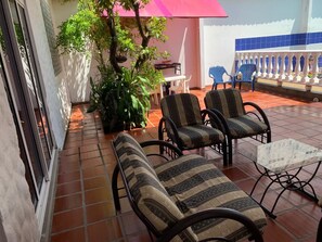 Une terrasse avec deux fauteuils rembourrés, une petite table et un pot de fleurs.