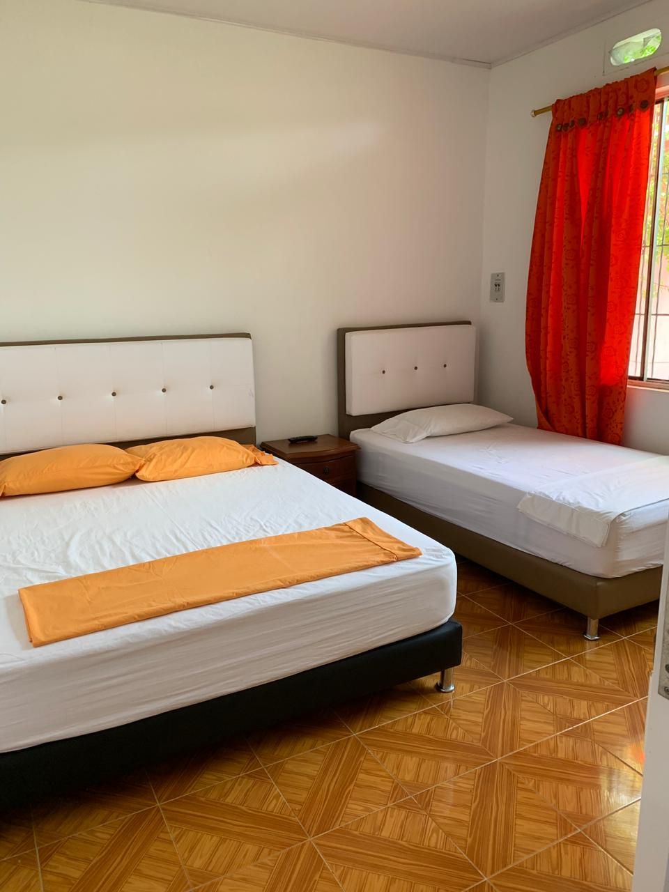 Quarto de hotel com duas camas, uma janela com cortinas vermelhas e chão de azulejos.