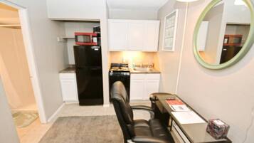 A compact kitchenette with a refrigerator, microwave, and stove, a dining area with a table and chairs, and a mirror on the wall.