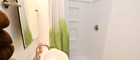 Un baño con un lavabo blanco, un espejo, una ducha con puerta blanca y un perchero con toallas marrones.