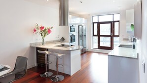 A modern kitchen with a central island, stainless steel appliances, and a large window providing natural light. - Hampden Apartments - The Charles (Windsor)