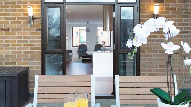 An outdoor seating area with a wooden table, two glasses of orange juice, a plate with croissants, and a potted orchid. - Hampden Apartments - The Charles (Windsor)