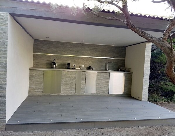 An outdoor kitchen with a built-in countertop, a coffee maker, and a sink.
