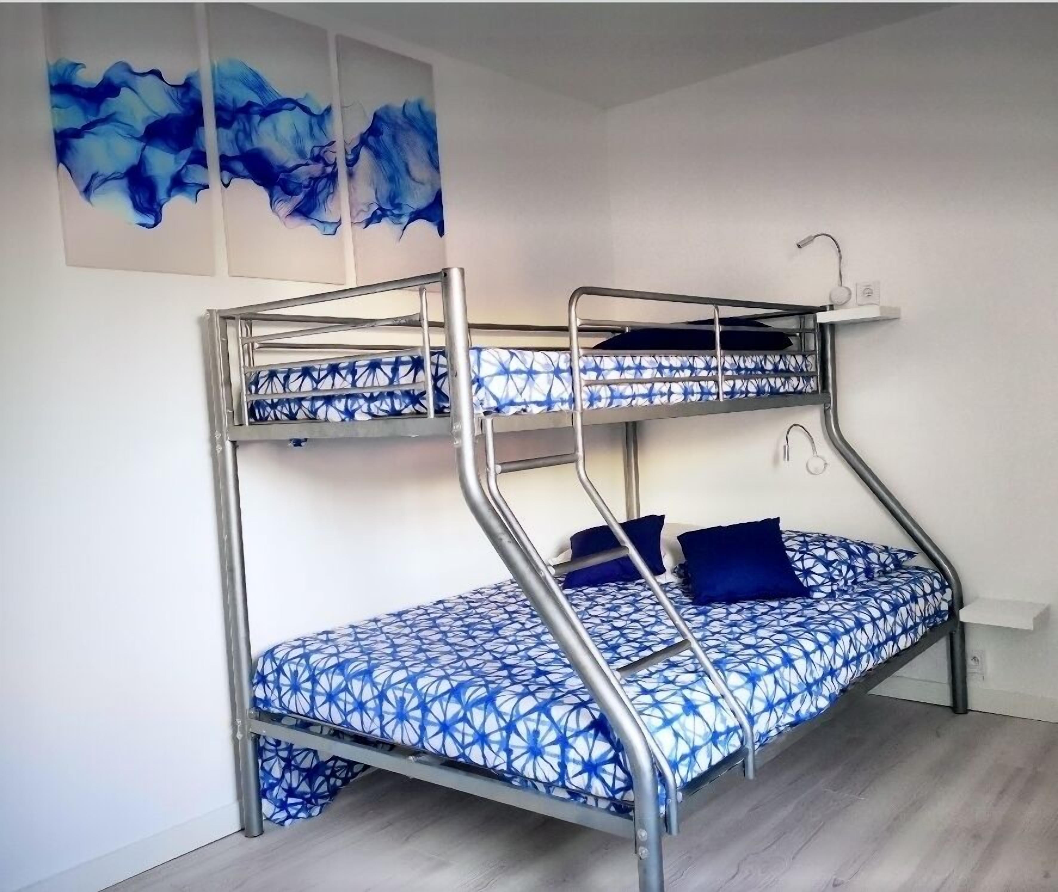 A bunk bed with a blue patterned mattress and pillows, a metal frame, and a wall-mounted light fixture.