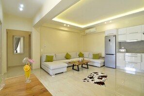 Relax in this stylish living space with a sofa, coffee table, and adjacent kitchen featuring a refrigerator and oven.