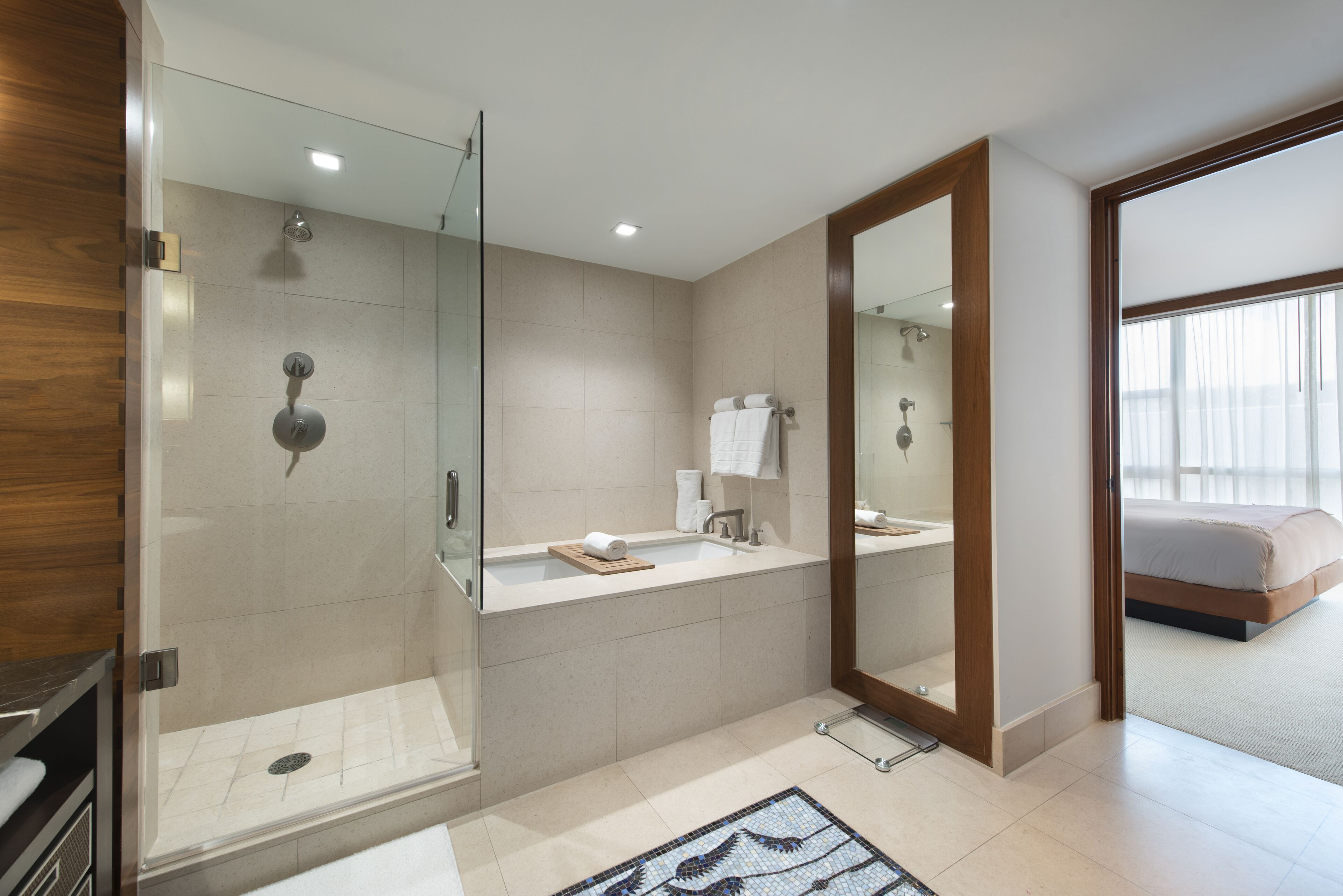 A modern bathroom with a glass-enclosed shower, a large mirror, and a separate sink area.