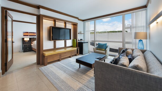 A modern hotel room with a large TV, a sofa, a coffee table, and a view of the city. - Large 2 BR 2 BA Apartment at The Carillon Wellness Resort (Miami Beach)