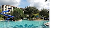 Relax by the resort pool surrounded by lush greenery and palm trees, featuring a multi-level water slide and lounge chairs.