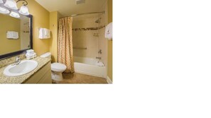 Bathroom features a sink, toilet, bathtub with showerhead, and toiletries on a shelf.