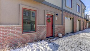 A row of townhouses with brick facades, red doors, and a snow-covered ground.