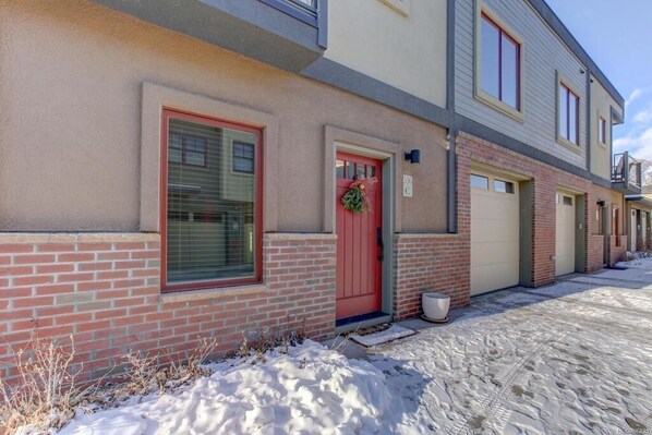 Un hilera de casas adosadas con fachadas de ladrillo, puertas rojas y un terreno cubierto de nieve.
