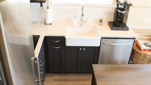 Una cocina compacta equipada con refrigerador, lavamanos, cafetera y una pequeña mesa de comedor.