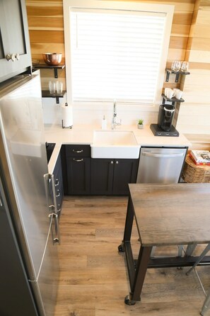 A compact kitchen with a refrigerator, sink, coffee maker, and a small dining table.