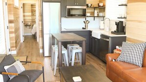 Un espacio habitable compacto con kitchenette, comedor y zona de estar con sofá y sillones.