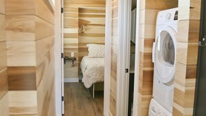 Un pasillo estrecho con paredes y suelos de madera, que conduce a un dormitorio con cama y lavadora.