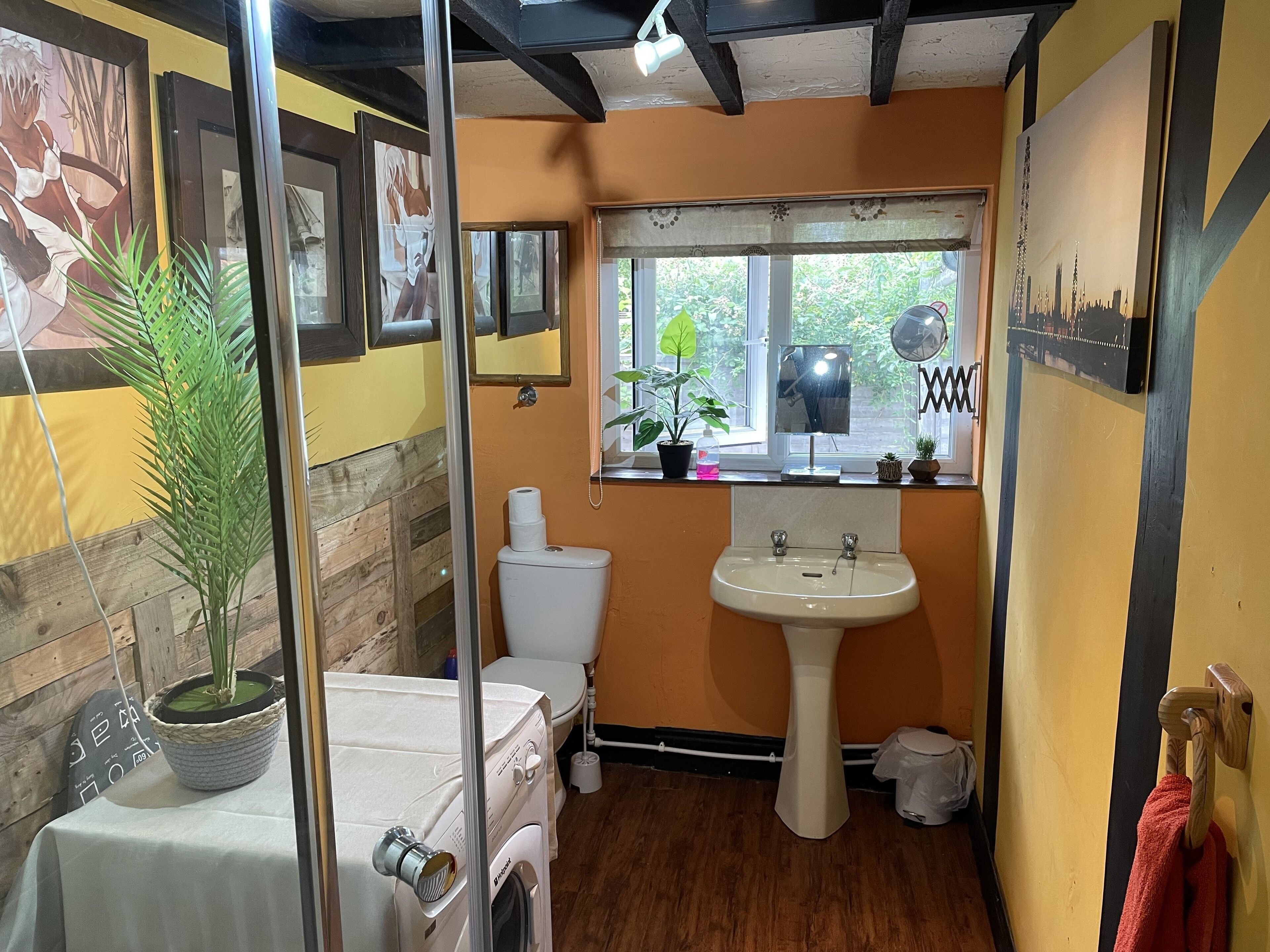 A compact bathroom with a toilet, sink, and a window with a view of greenery.