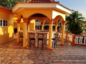 A covered outdoor seating area with a stone-tiled floor, a central table, and four chairs.