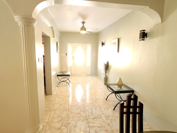 A hallway with a marble floor, a ceiling fan, and a table with a vase.