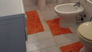Ein Badezimmer mit Waschbecken, Bidet und Toilette. Der Boden ist mit orangefarbenen Teppichen ausgelegt.
