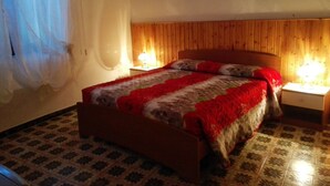 Ein Schlafzimmer mit einem hölzernen Kopfteil, einem Bett mit roter und weißer Decke, zwei Nachttischlampen und einem Fußboden mit Mustertrennung.