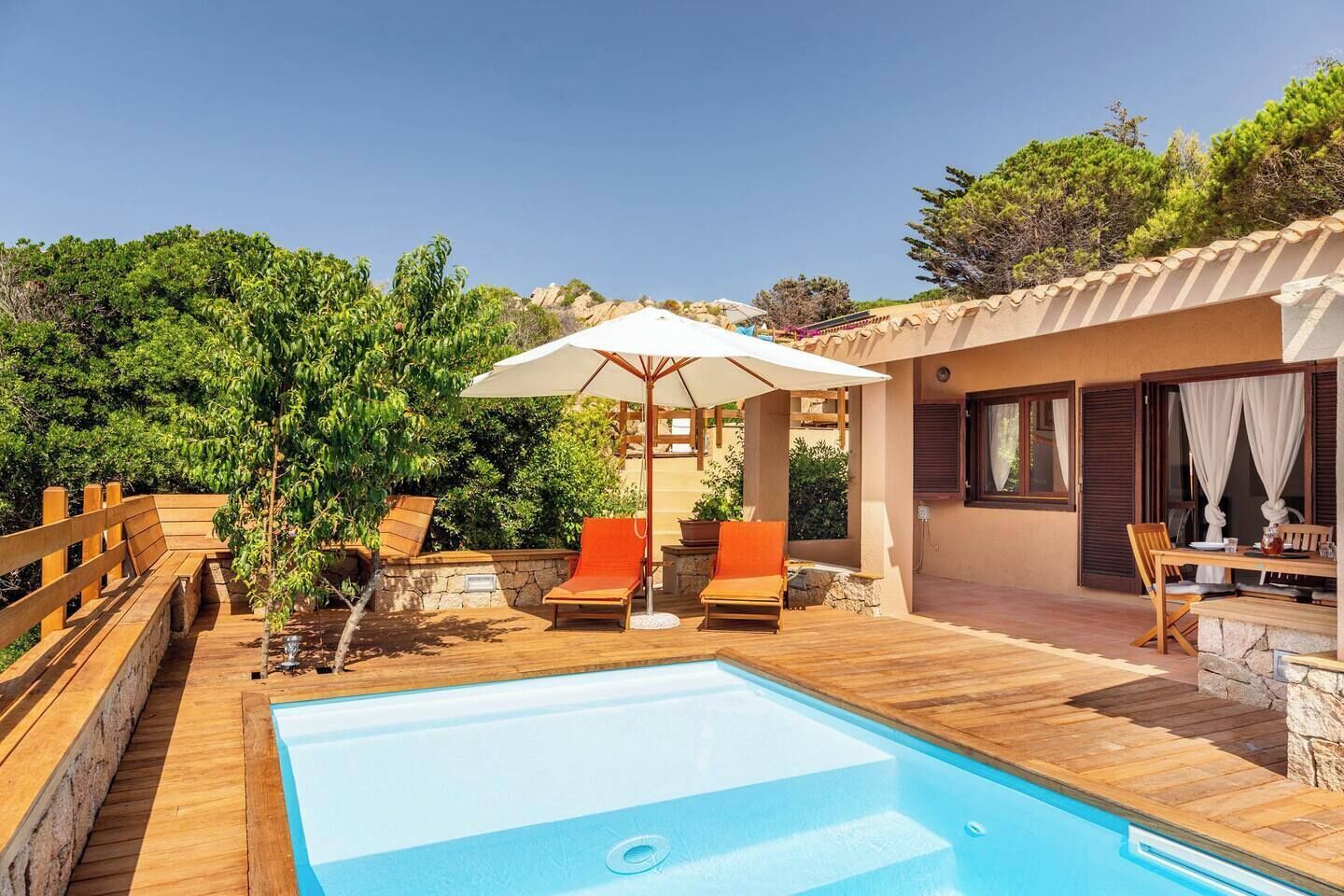 A pool area with wooden deck, lounge chairs, and a pergola with an umbrella.