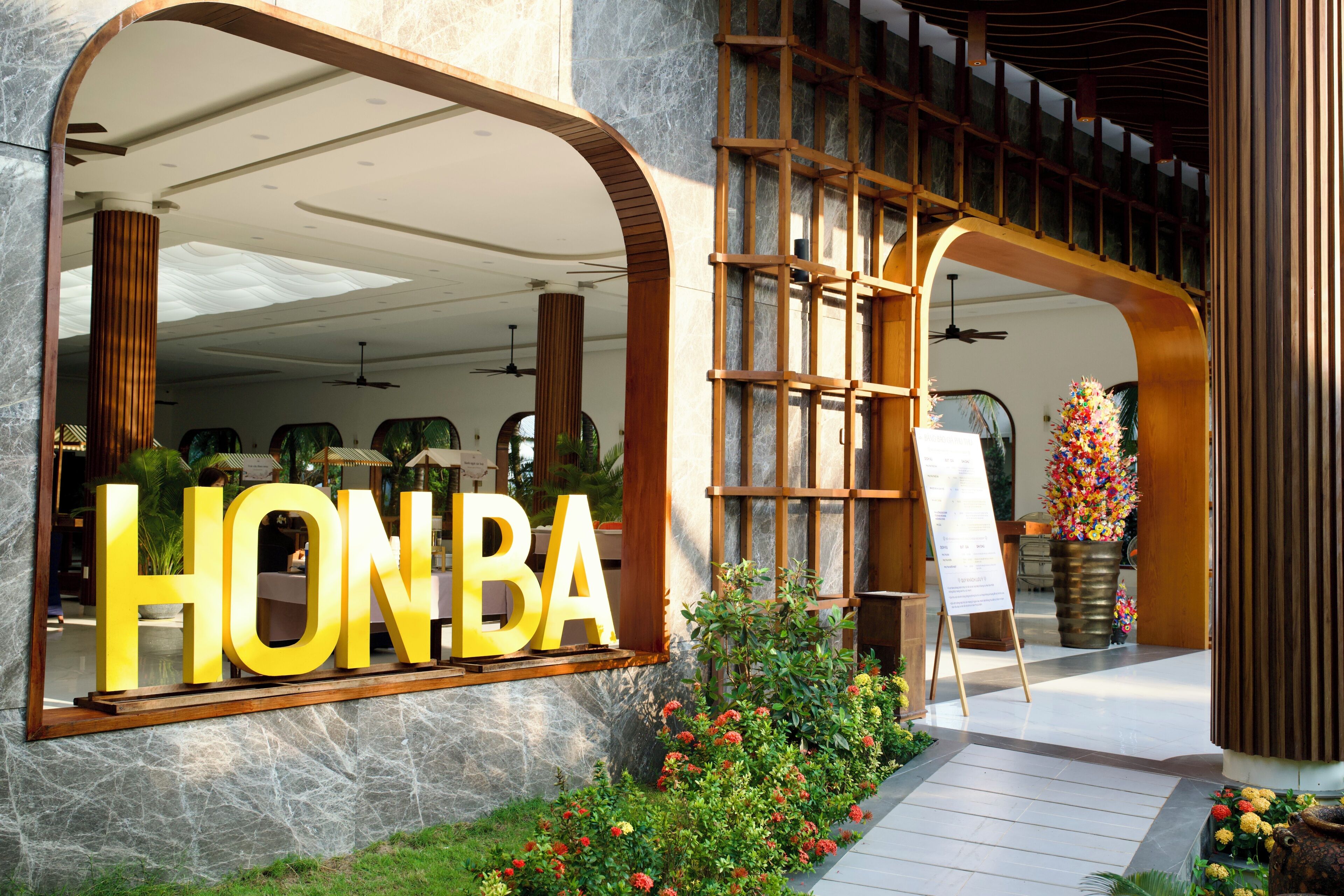 L’entrée d’un hôtel, avec une grande enseigne « HONBA », une arche en bois et une composition florale.