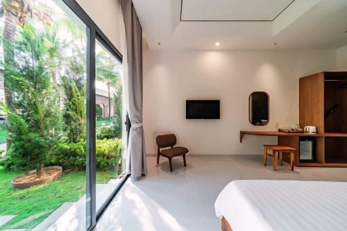 Habitación de hotel moderna con un ventanal grande, una cama, un televisor, un escritorio de madera y una silla.