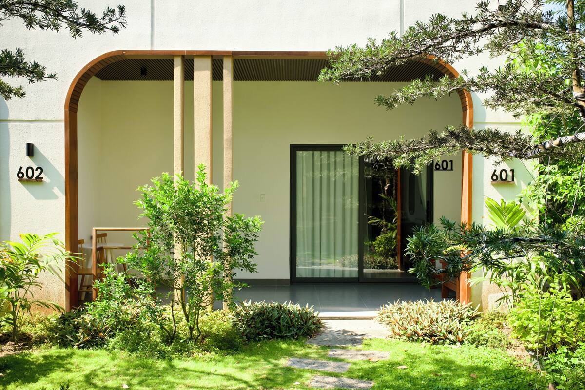 Un edificio moderno con una amplia entrada en arco, números 602 y 601, rodeado de abundante vegetación y un sendero de piedra.