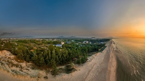 A coastal landscape with a beach, a small settlement, and distant mountains. - Honba Lagi Beach Resort (La Gi)