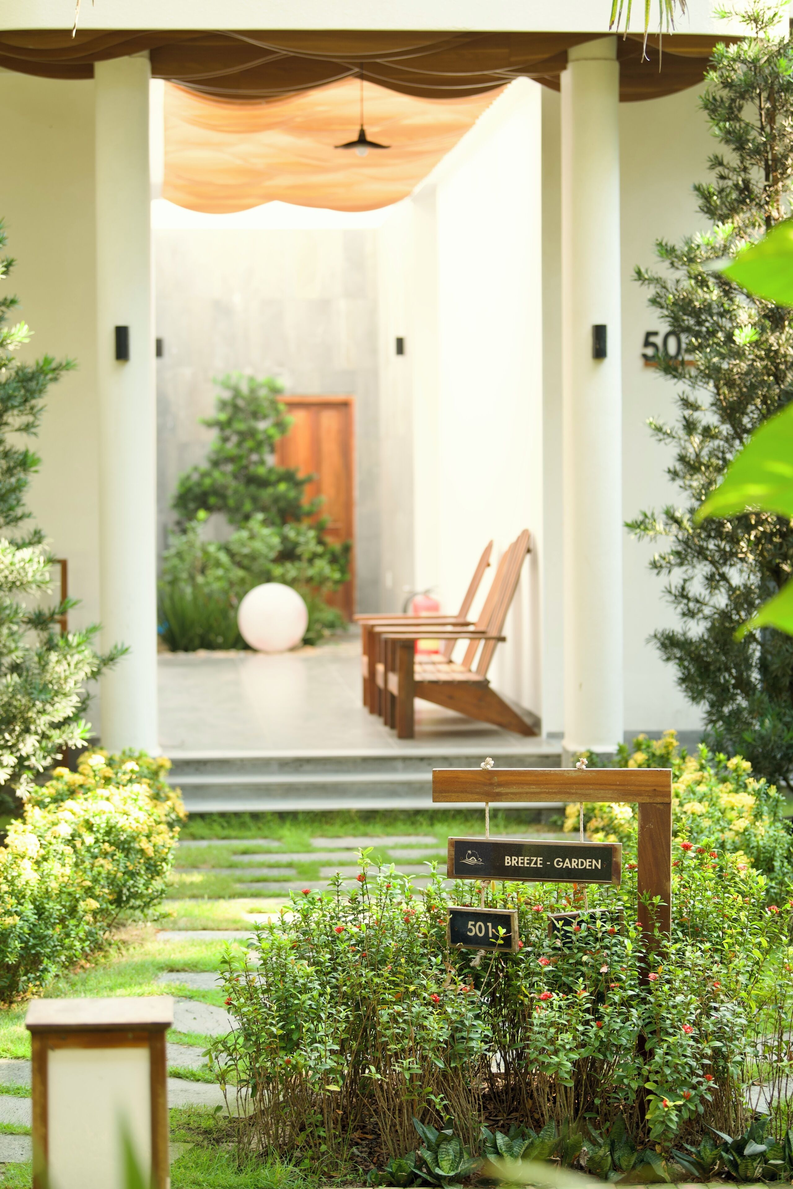 Una entrada de jardín con un banco de madera, un adorno esférico y un letrero que indica 'BREEZE - GARDEN' y '501'.