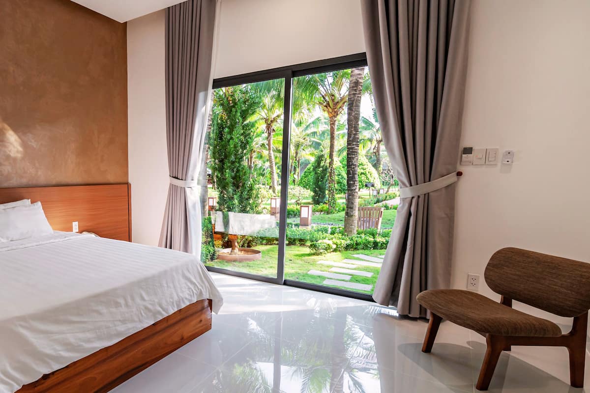Un dormitorio con cama, una silla y vistas a un jardín a través de un ventanal grande.