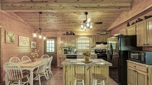 Cocina estilo cabaña de madera con una isla central, sillas blancas y una mesa de comedor.