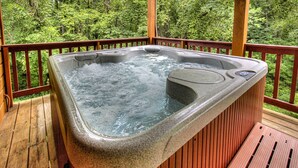 Un jacuzzi en una terraza de madera con un bosque al fondo.