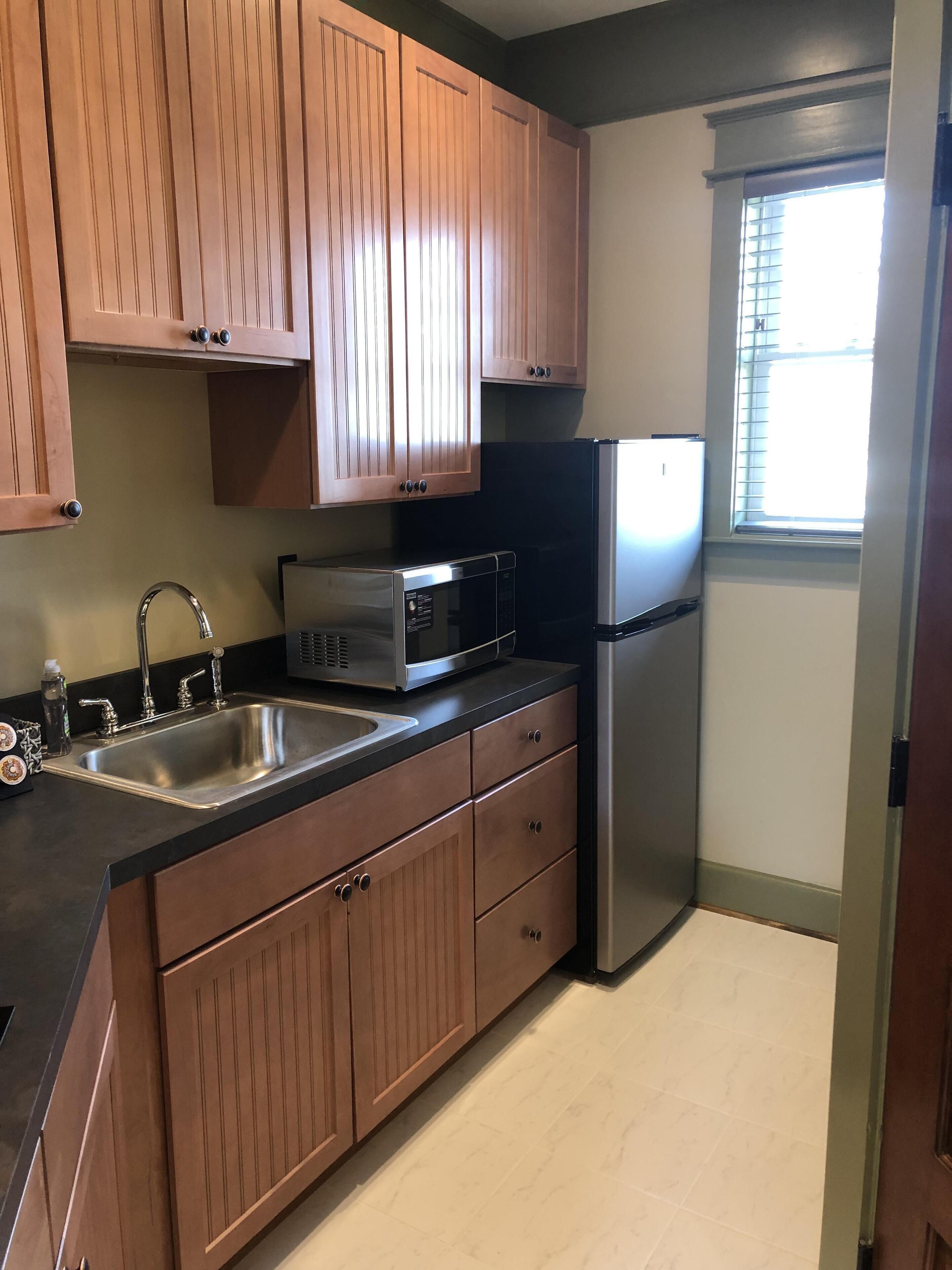 A compact kitchen with wooden cabinets, a stainless steel sink, a microwave, and a refrigerator.