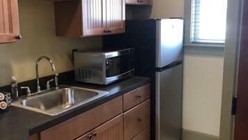 A compact kitchen with wooden cabinets, a stainless steel sink, a microwave, and a refrigerator.