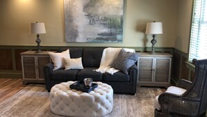 A living room with a dark grey sofa, a white tufted ottoman, a black wicker chair, and two side tables with lamps. A large abstract painting hangs on the wall. - Guest quarters at the inn - 205 (North Beach)